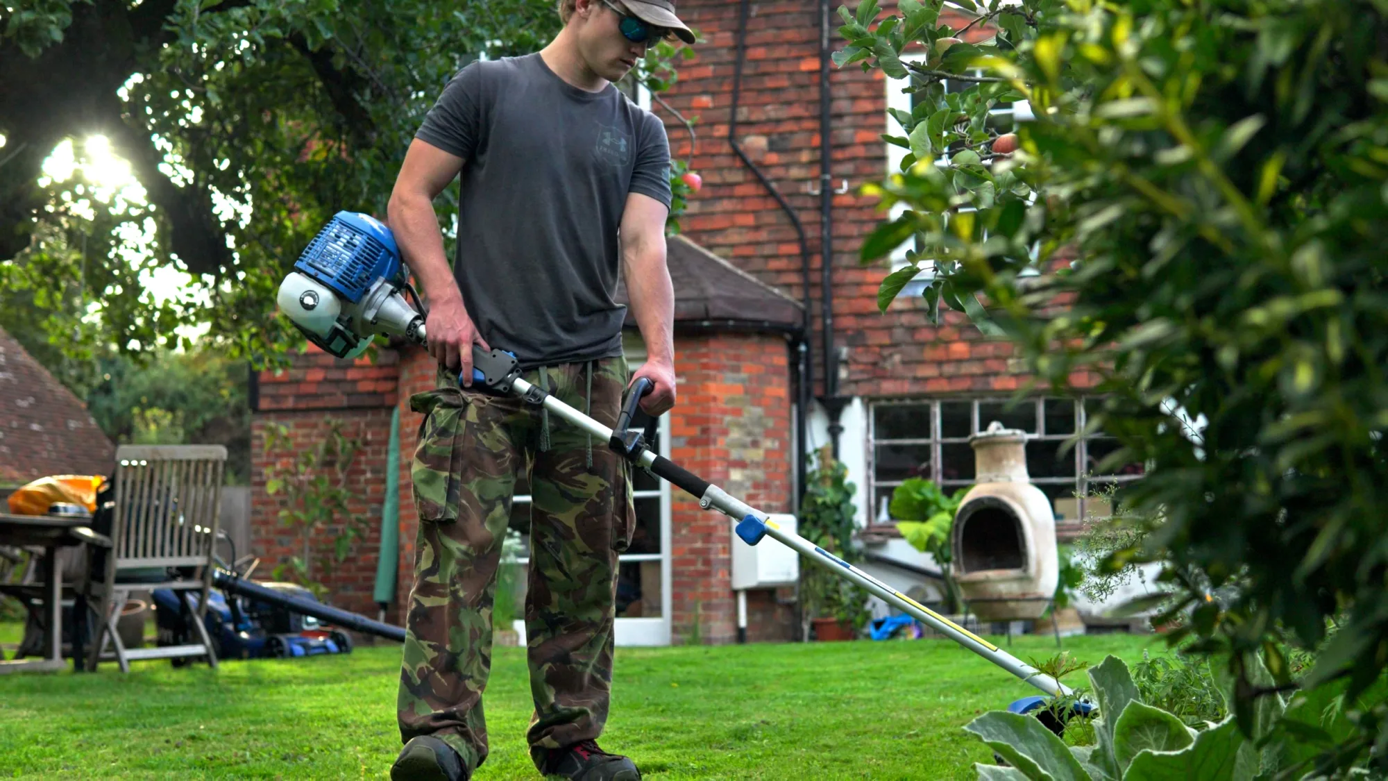 Strimming the edge of a lawn in front of a brick house